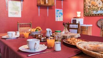 Une table de petit-déjeuner dressée avec des tasses, un pichet, un verre de jus d’orange, un panier de croissants et un pot de confiture.