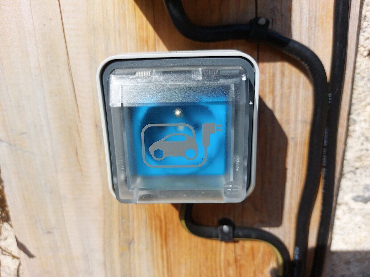 Une borne de recharge pour voitures, dotée d’une icône bleue et reliée à un câble noir.