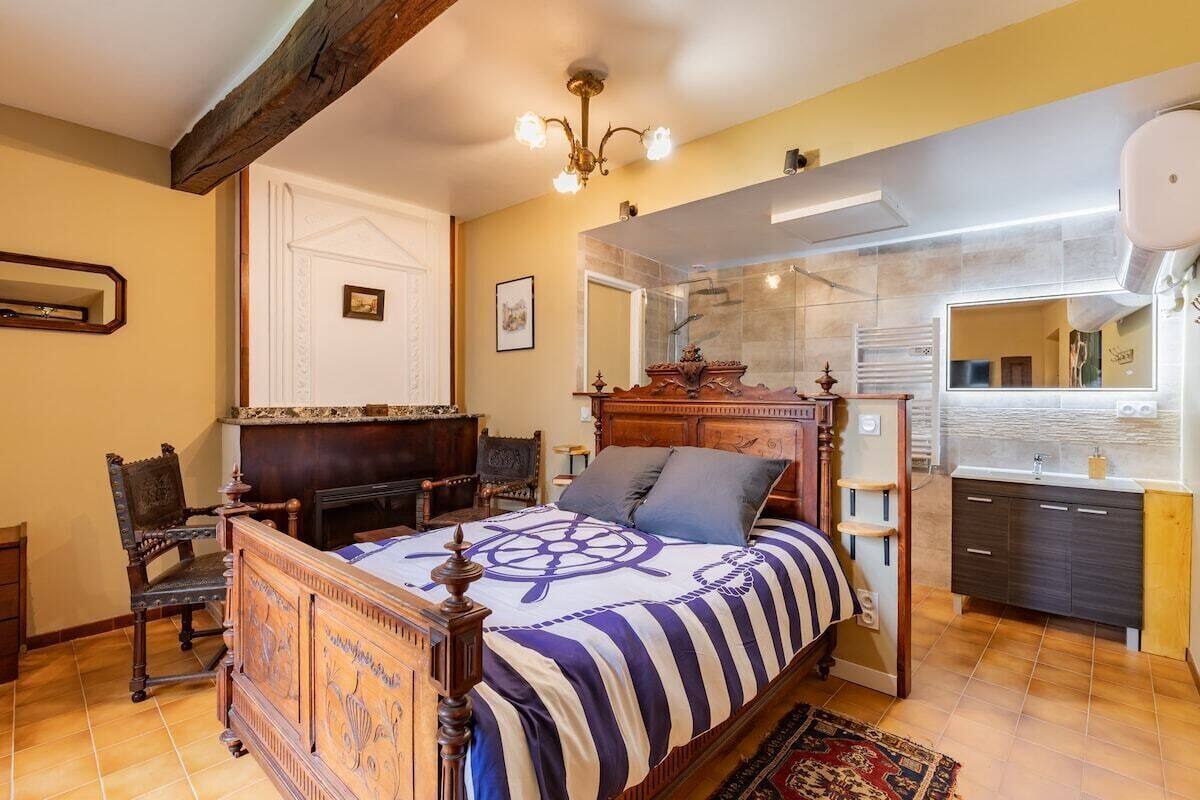 A bedroom with a wooden bed, a large mirror, a built-in wardrobe, and a bathroom with a shower and sink.