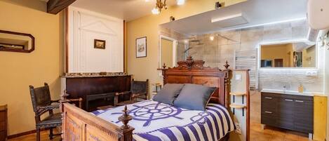 A bedroom with a wooden bed, a large mirror, a built-in wardrobe, and a bathroom with a shower and sink.