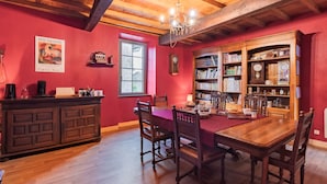 Un comedor con una mesa y sillas de madera, una araña y una estantería llena de libros y objetos decorativos.