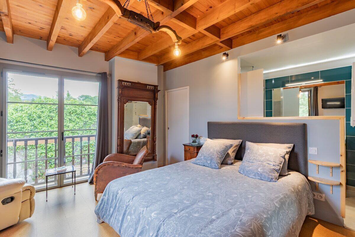 A bedroom with a large bed, a wooden ceiling, a balcony with a view, and a mirror.