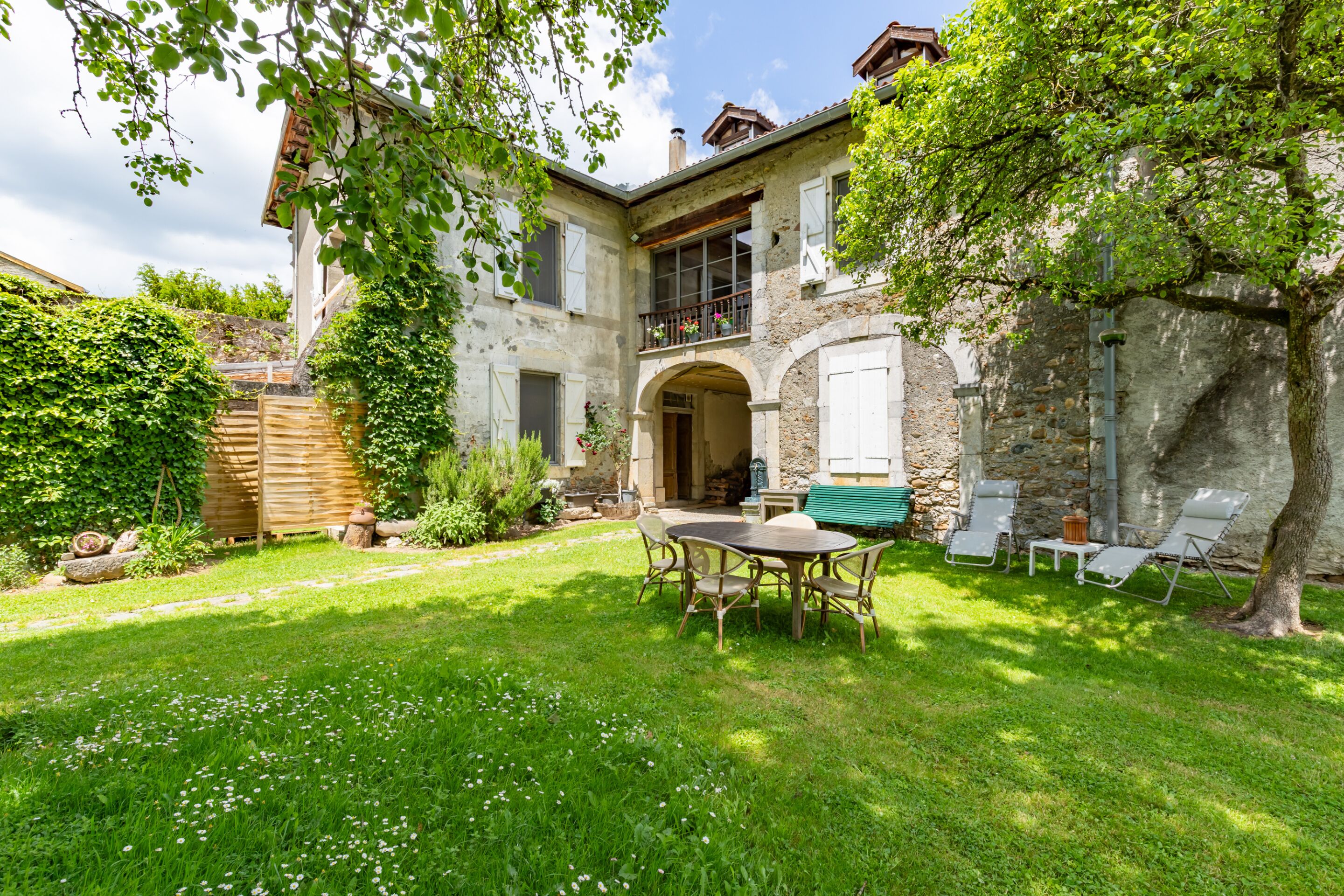 A two-story stone house with a balcony, a wooden deck, and a grassy yard.