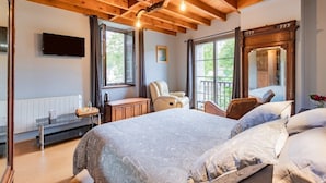 Un dormitorio con una cama grande, vigas de madera en el techo, un televisor y una ventana con vistas a zonas verdes.