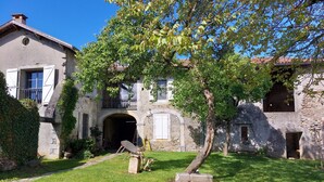 Un edificio rústico de piedra con un patio cubierto, un árbol y un pequeño jardín.