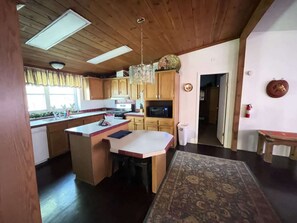 Une cuisine avec des meubles en bois, un îlot central, un four à micro-ondes et un lustre.