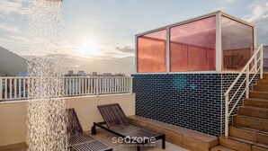 A balcony with a water feature, a wooden chair, and a view of the sunset. - PVI - Charming Apartments Just 450m From the Seafront in Ubatuba/sp (Ubatuba)
