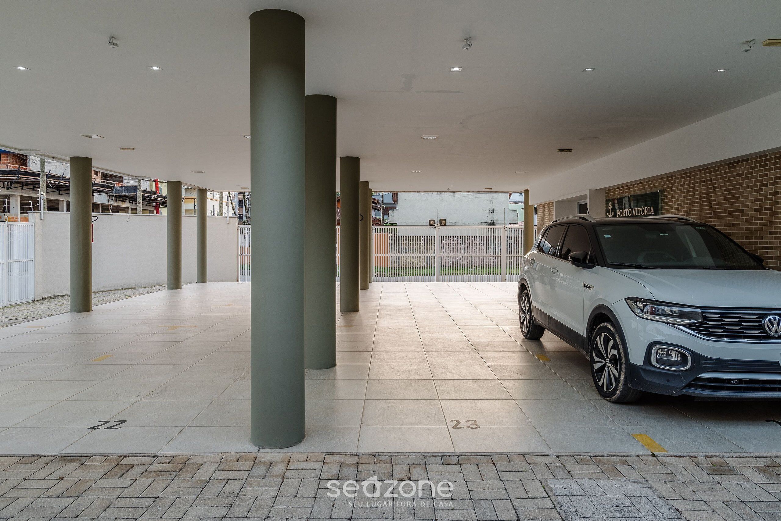 A covered parking area with numbered parking spaces, a white SUV parked, and a sign reading "Porto Vitória".
