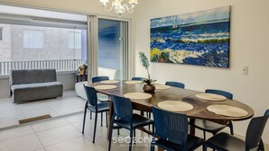 A dining area with a wooden table, blue chairs, and a painting of a seascape. - PVI - Charming Apartments Just 450m From the Seafront in Ubatuba/sp (Ubatuba)