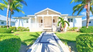 A white two-story house with a front porch, palm trees, and a well-maintained lawn. - Exclusive Bimini Bay home with private boat slip. (Bimini)