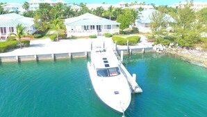 A marina with a white boat docked at a pier, surrounded by residential buildings and greenery. - Exclusive Bimini Bay home with private boat slip. (Bimini)