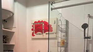 A bathroom with a toilet, a glass shower enclosure, and a shelf with toiletries. - Your apartment with free prking in St Etienne (Saint-Étienne)