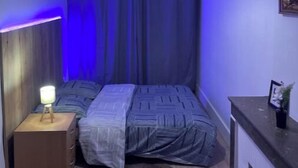A small bedroom with a bed, a nightstand, a red hanging light, and a painting on the wall. - Your apartment with free prking in St Etienne (Saint-Étienne)