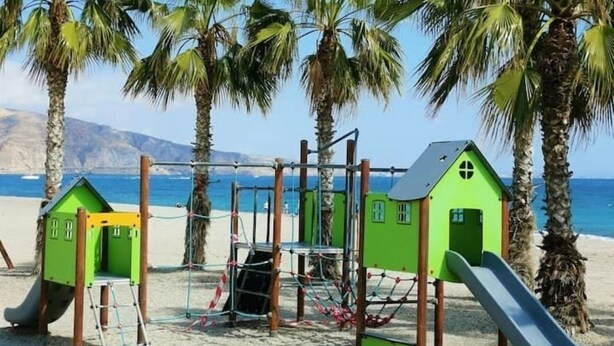 A beach playground with green play structures and a slide.