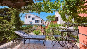 Un patio con mesa y sillas, una pérgola y vistas a una casa blanca con techo rojo.