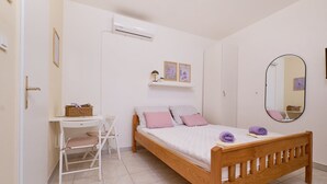 Un dormitorio con una cama de madera, un escritorio, una silla, una estantería con fotos y un espejo.