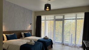 Quarto de hotel com duas camas, piso de madeira, uma janela grande com cortinas e um lustre.