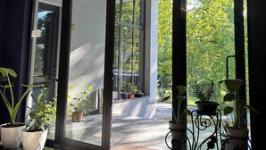 Entrada de hotel com porta de vidro, plantas em vasos e vista para o exterior.