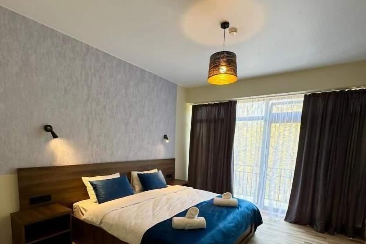 Un dormitorio con una cama de madera, una mesita de noche, una lámpara de pared y una ventana con cortinas.