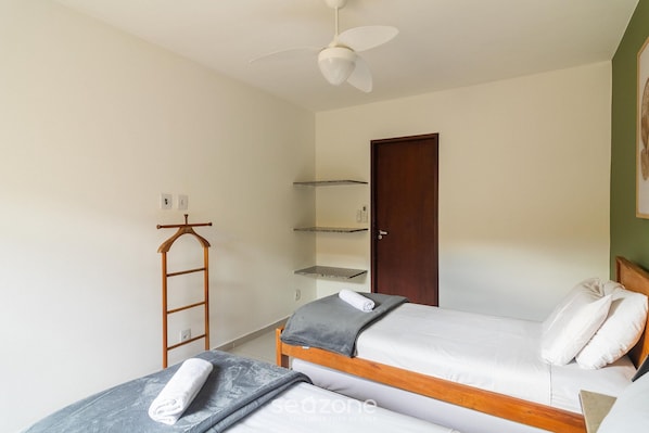 Une chambre avec deux lits simples, une échelle en bois, un ventilateur de plafond et une porte.