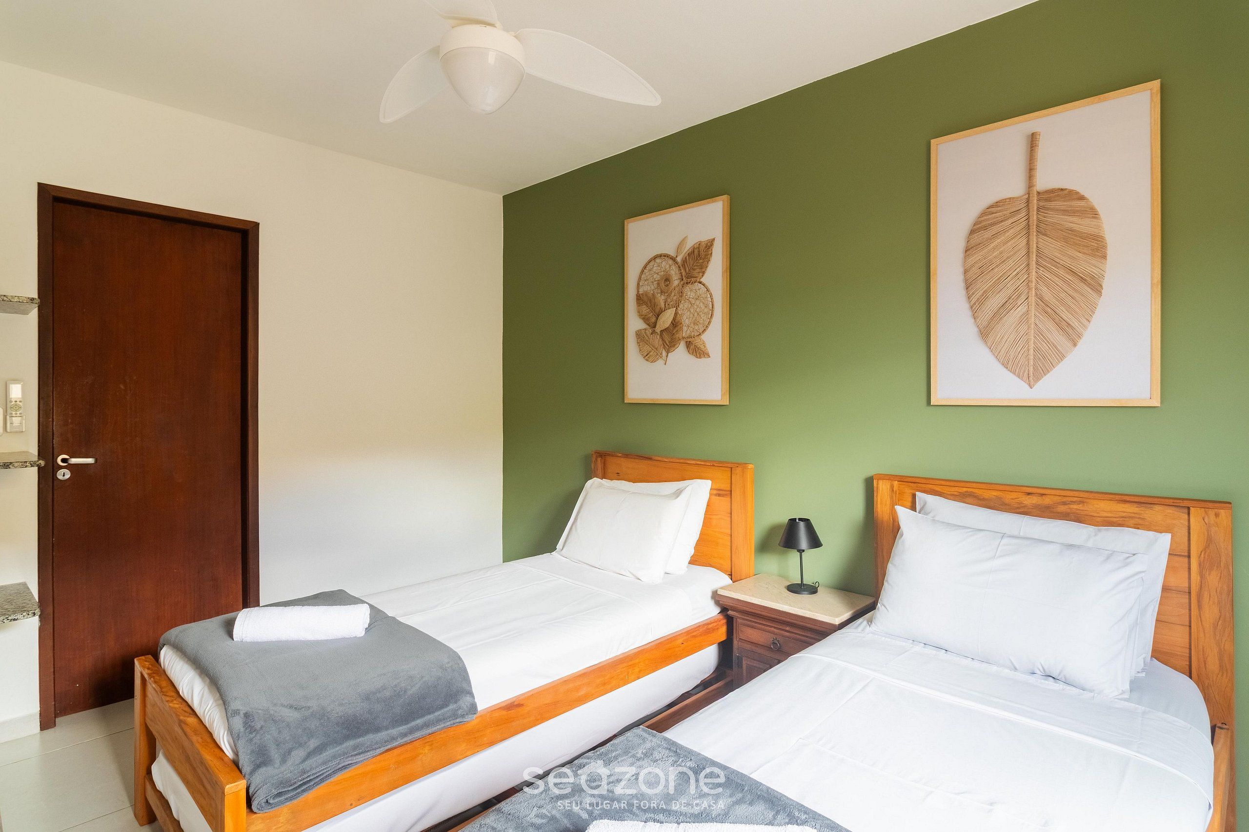 A bedroom with two beds, a wooden headboard, a nightstand with a lamp, and framed artwork on the wall.