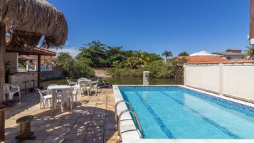A swimming pool with a thatched roof and outdoor seating area.