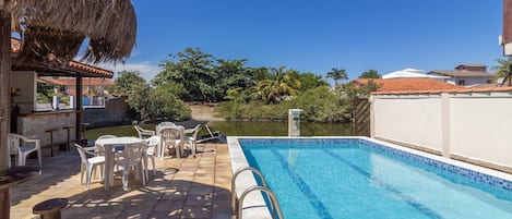 A swimming pool with a thatched roof and outdoor seating area.