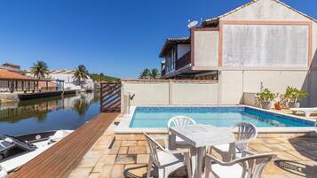 A pool area with a wooden deck, white chairs, and a table.