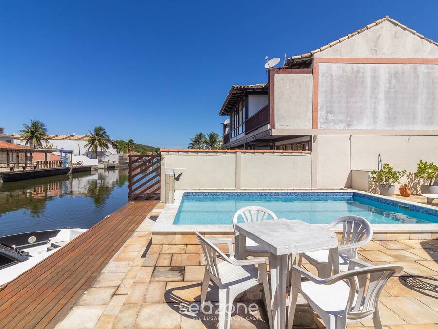A pool area with a wooden deck, white chairs, and a table.