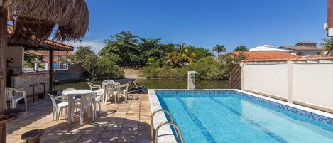 Piscina con techo de paja y zona de estar al aire libre.