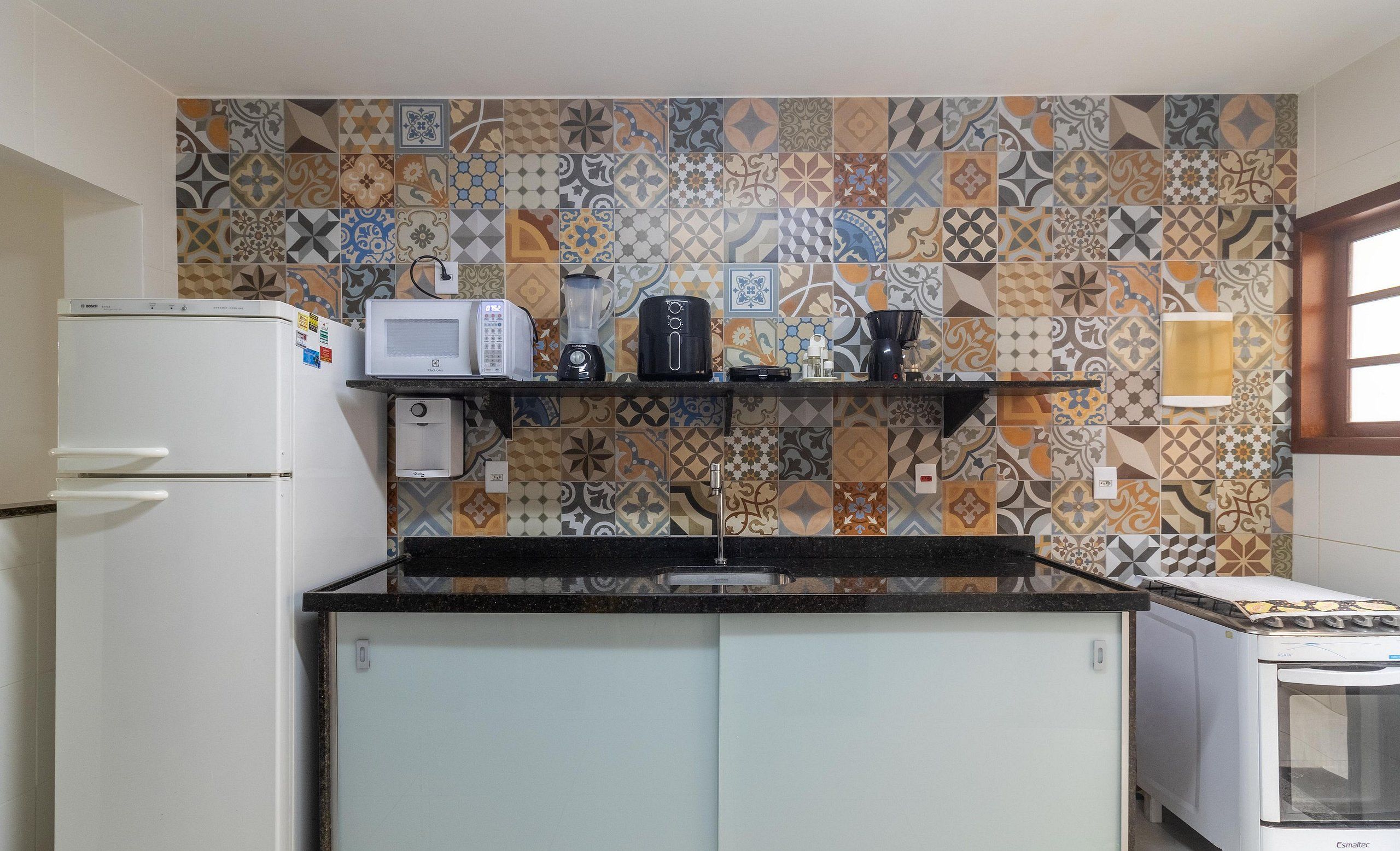 A compact kitchen with a microwave, coffee maker, and toaster on a shelf, a refrigerator, and a sink.