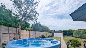 Un jacuzzi en un patio trasero con cerco de madera, un cobertizo pequeño y un seto.