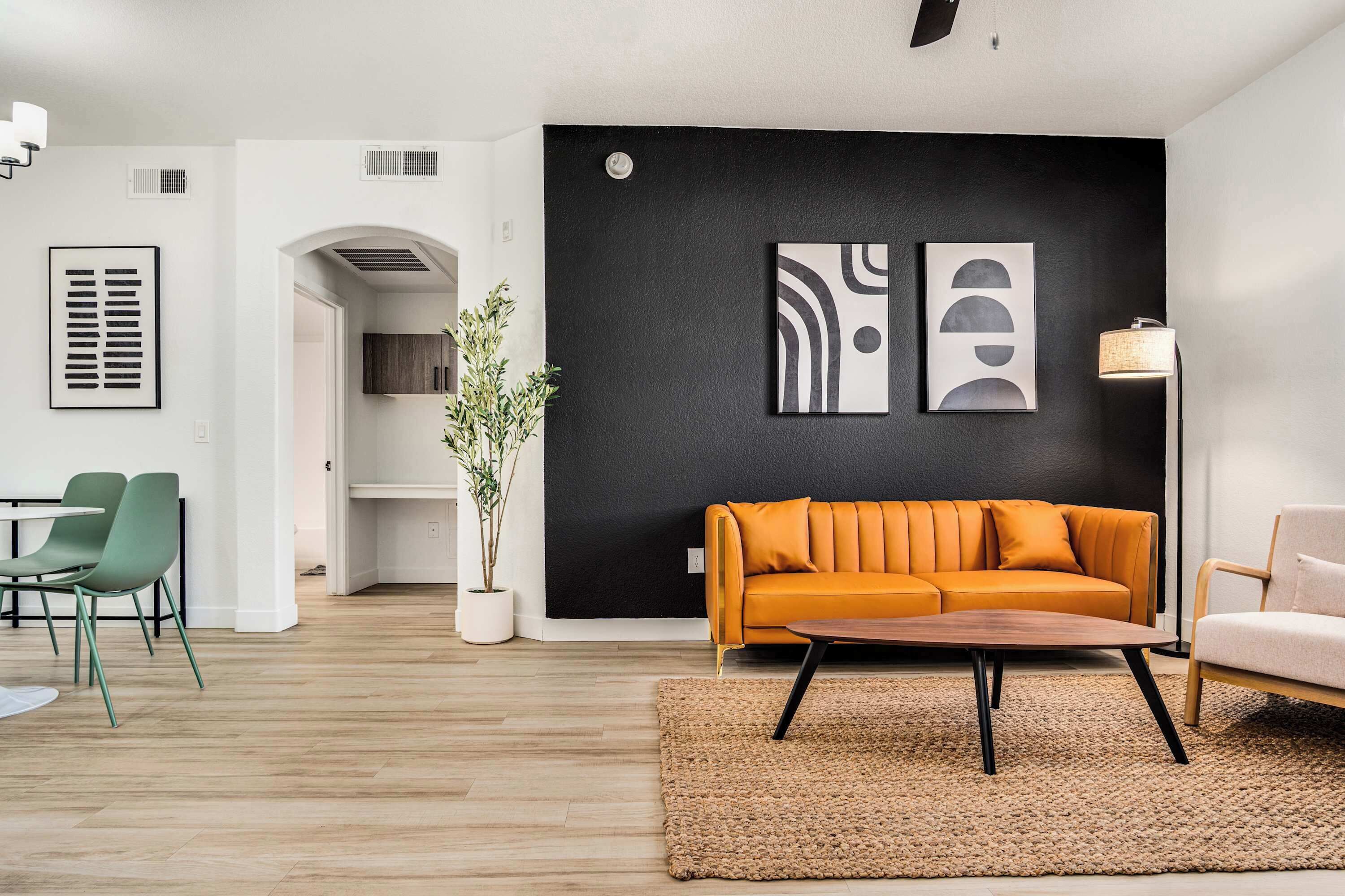 A modern living room with a sofa, coffee table, and chairs, a black accent wall with artwork, and a potted plant.