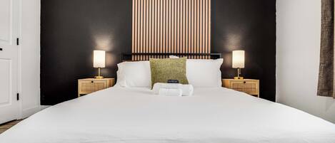 Una cama bien hecha con sábanas blancas, dos lámparas de noche y una pared con rayas verticales.