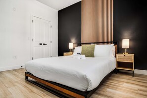 Una habitación de hotel moderna con una cama grande, dos mesitas de noche, una lámpara de pared y una puerta.
