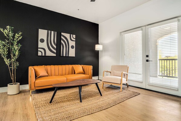 Una sala de estar moderna con sofá, sillón y mesa de centro, una planta en maceta y arte abstracto en la pared.