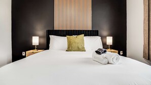 A neatly made bed with white linens, a green pillow, and a rolled towel on the side. There are two bedside lamps on wooden nightstands.