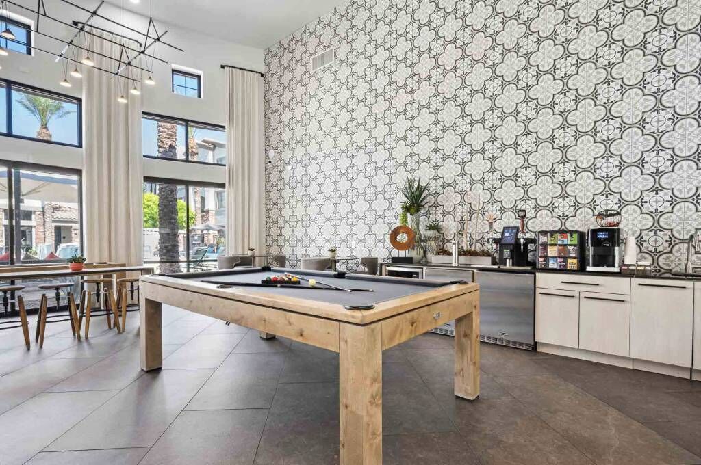 A modern indoor pool area with a pool table, bar seating, and a kitchen area with a patterned backsplash.