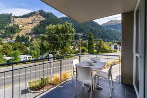 A balcony with a table and chairs, overlooking a road and a mountainous landscape.