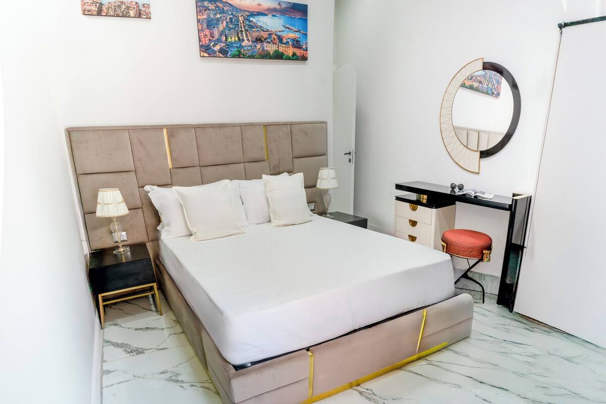 A neatly arranged bedroom with a large bed, bedside tables, a desk, and a mirror.