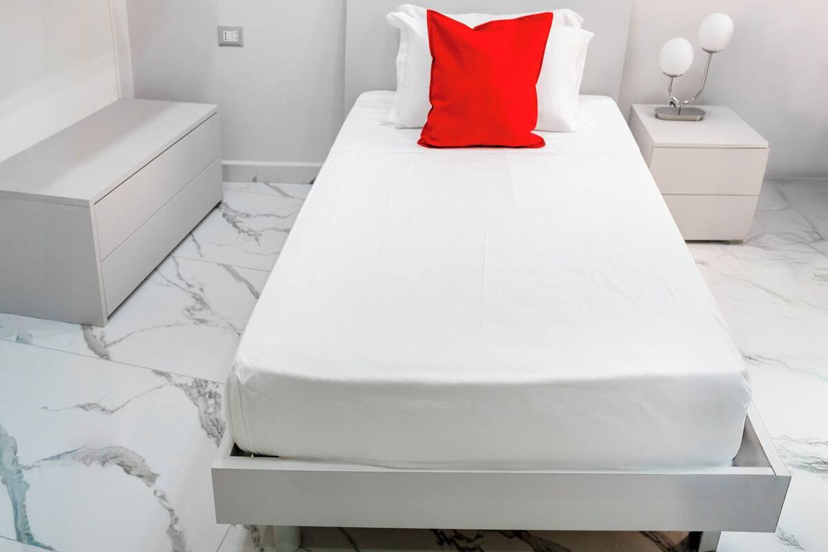 A modern bedroom with a bed, white nightstands, and a marble floor.