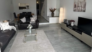 A modern living room with a black leather sofa, a coffee table, and a TV stand. - Golf Course House with 3 Terraces, heated pool, tennis acess, near beach (Marbella)