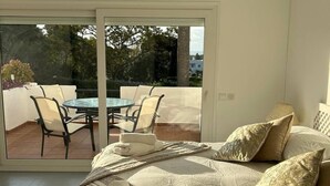 A bedroom with a large bed, a view of an outdoor patio with a table and chairs, and a sliding glass door leading to the patio. - Golf Course House with 3 Terraces, heated pool, tennis acess, near beach (Marbella)