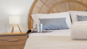 Una cama con cabecera de mimbre, una lámpara de noche y una taza sobre la mesita.