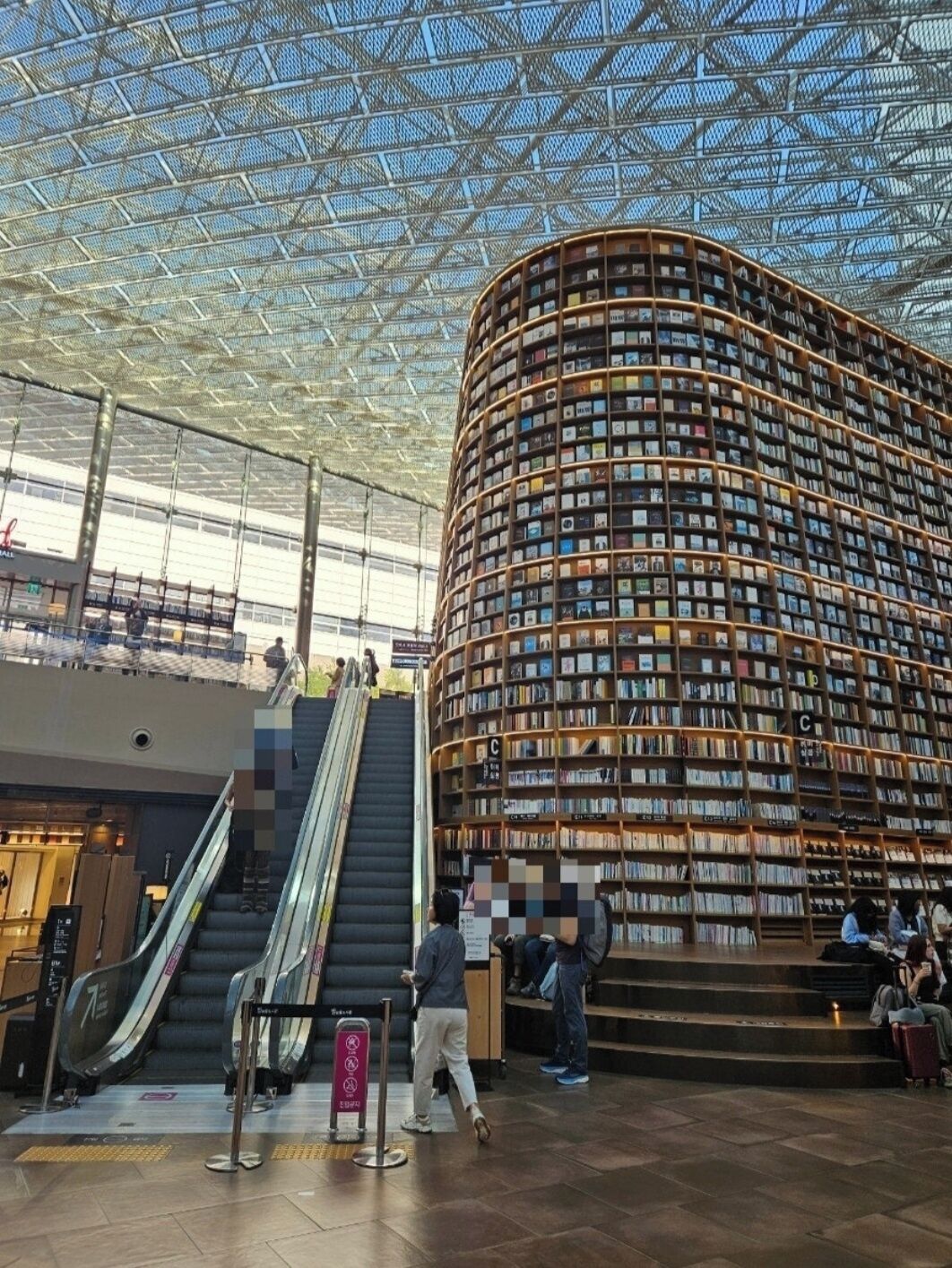 Uma biblioteca moderna com uma estrutura de estante curva, uma escada rolante e um teto de vidro.