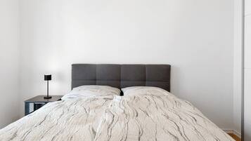 Una cama con una colcha texturizada, un cabecero oscuro y una mesita de noche pequeña con una lámpara.