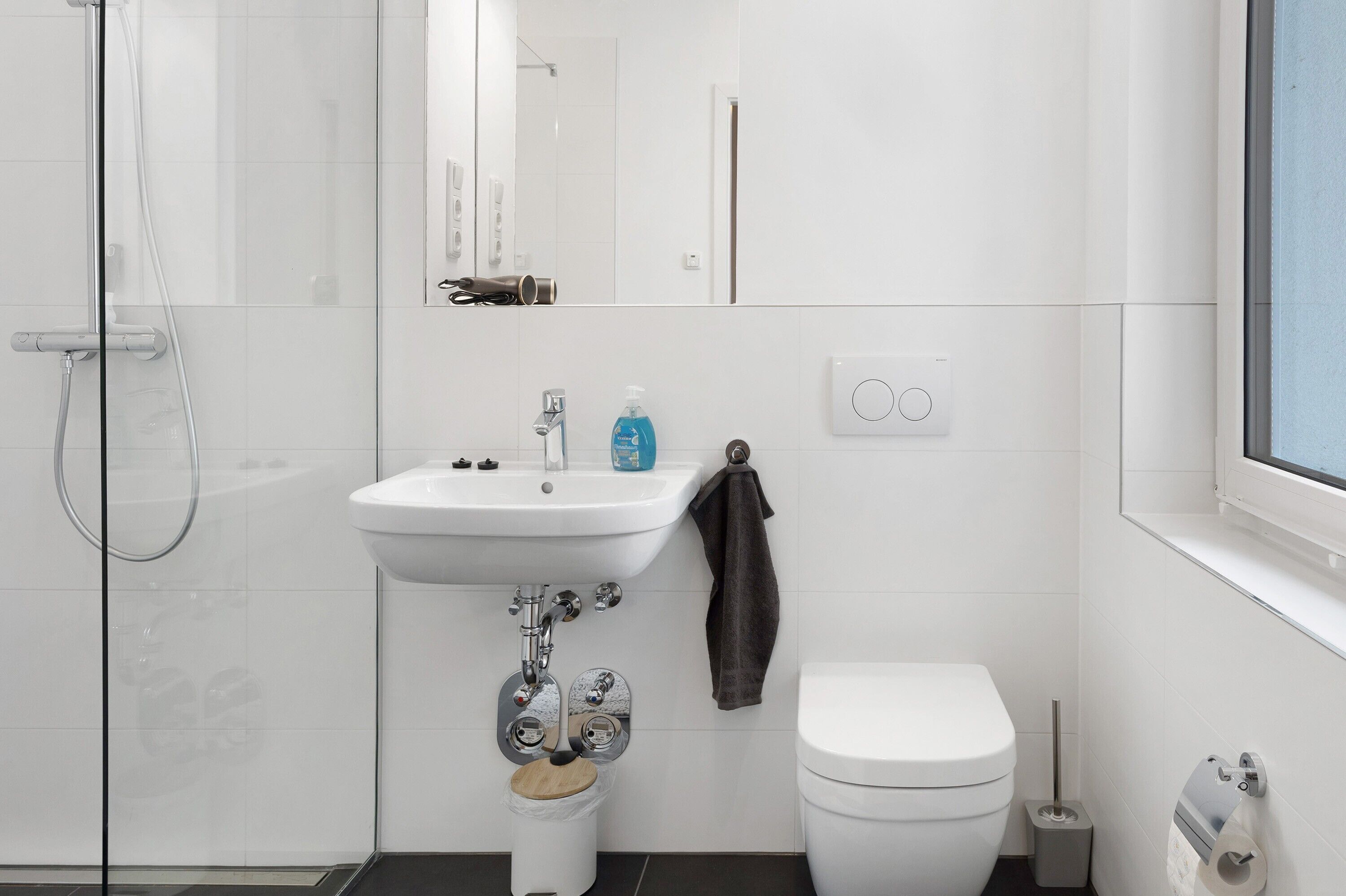 Un bany modern amb plat de dutxa de vidre, un lavabo blanc amb mirall a sobre, vàter i barra de tovalloles.