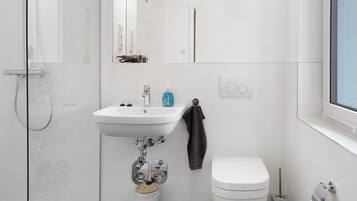 Un bany modern amb plat de dutxa de vidre, un lavabo blanc amb mirall a sobre, vàter i barra de tovalloles.
