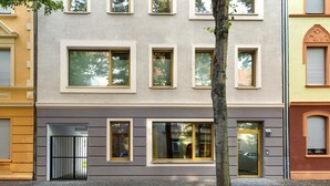 A multi-story building with a modern facade, large windows, and a tree in front.