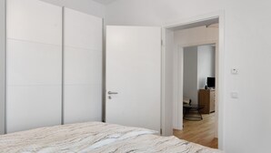 A bedroom with a bed, a wardrobe, and an open door leading to a dining area with a table and chairs.